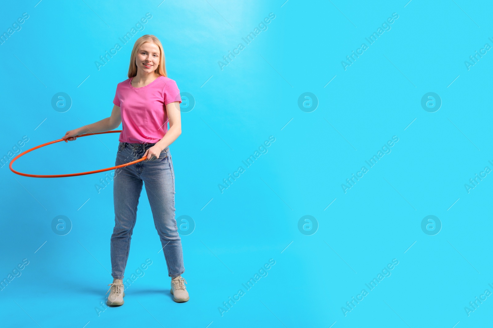 Photo of Beautiful young woman exercising with hula hoop on light blue background, space for text