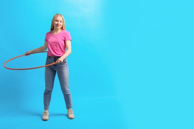 Beautiful young woman exercising with hula hoop on light blue background, space for text