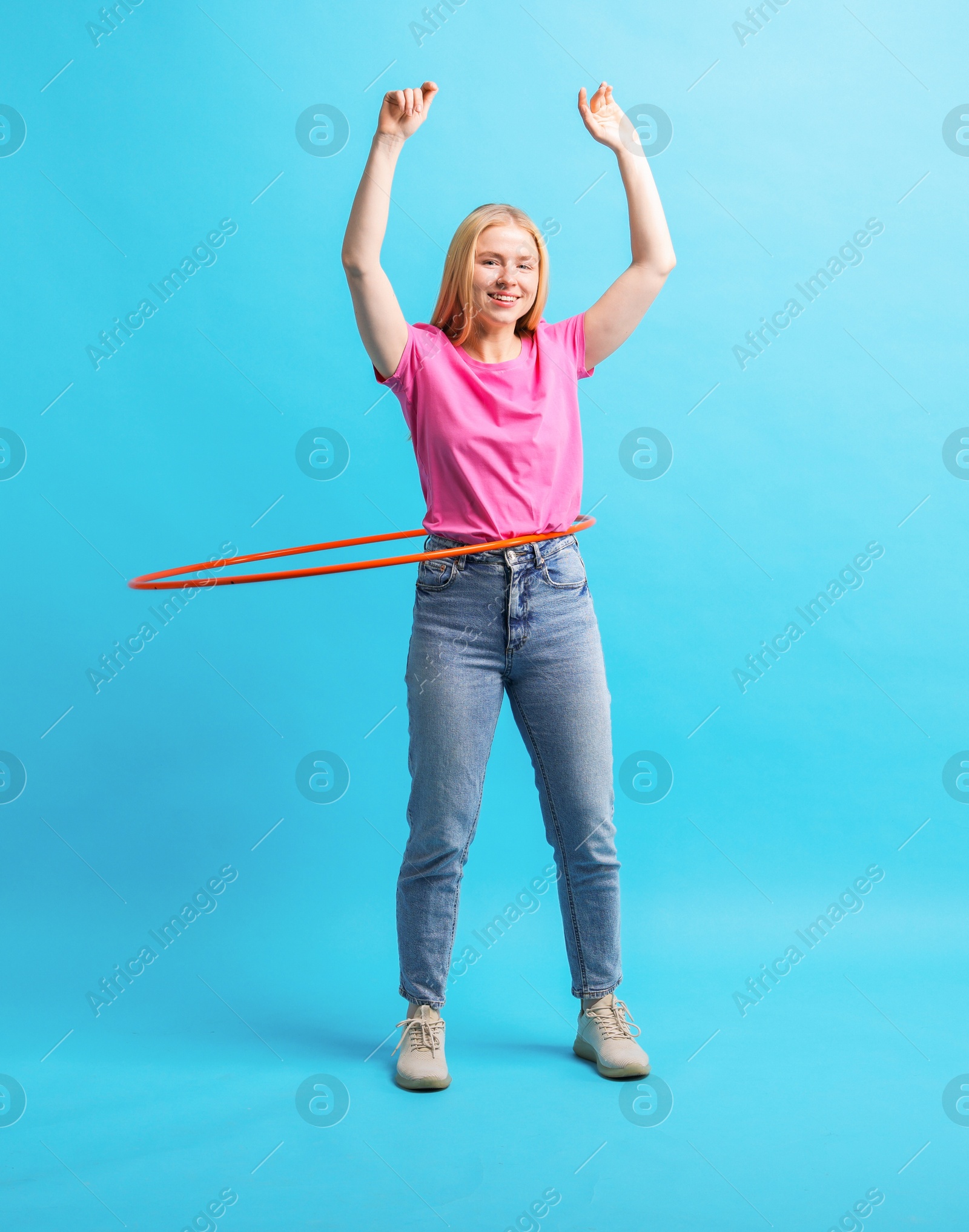 Photo of Beautiful young woman exercising with hula hoop on light blue background