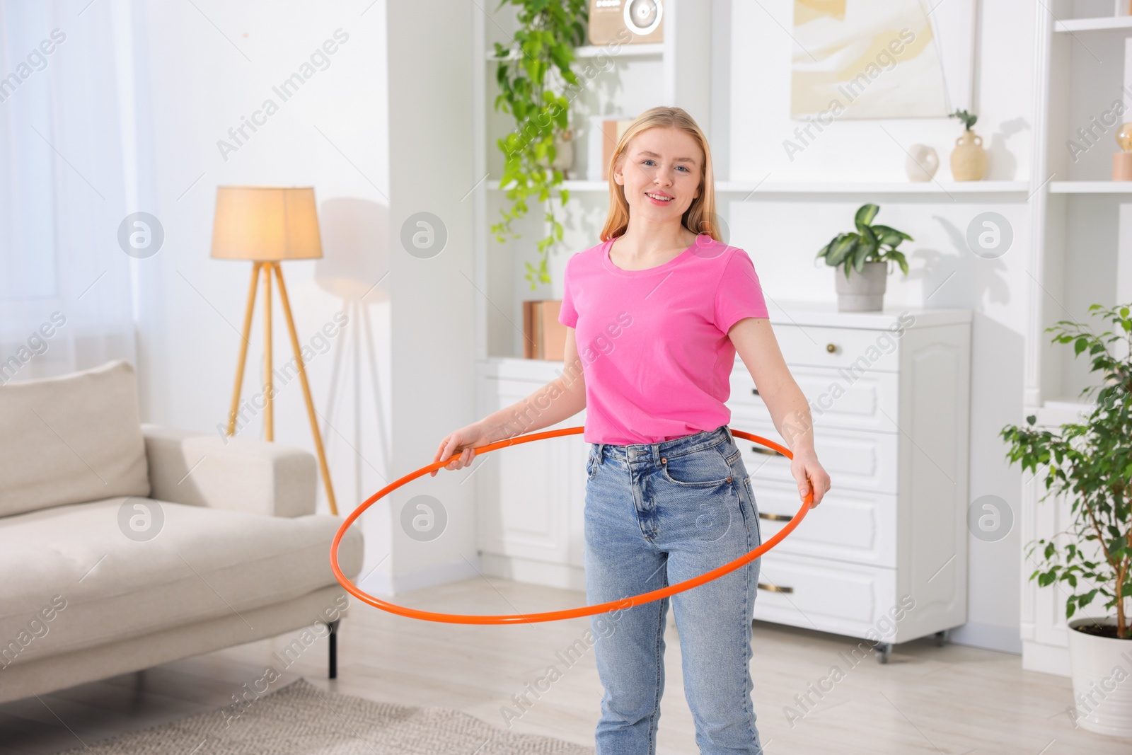 Photo of Beautiful young woman exercising with hula hoop at home