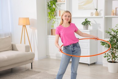 Photo of Beautiful young woman exercising with hula hoop at home