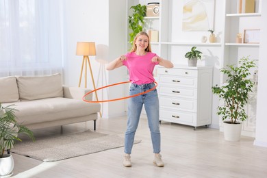 Beautiful young woman exercising with hula hoop at home