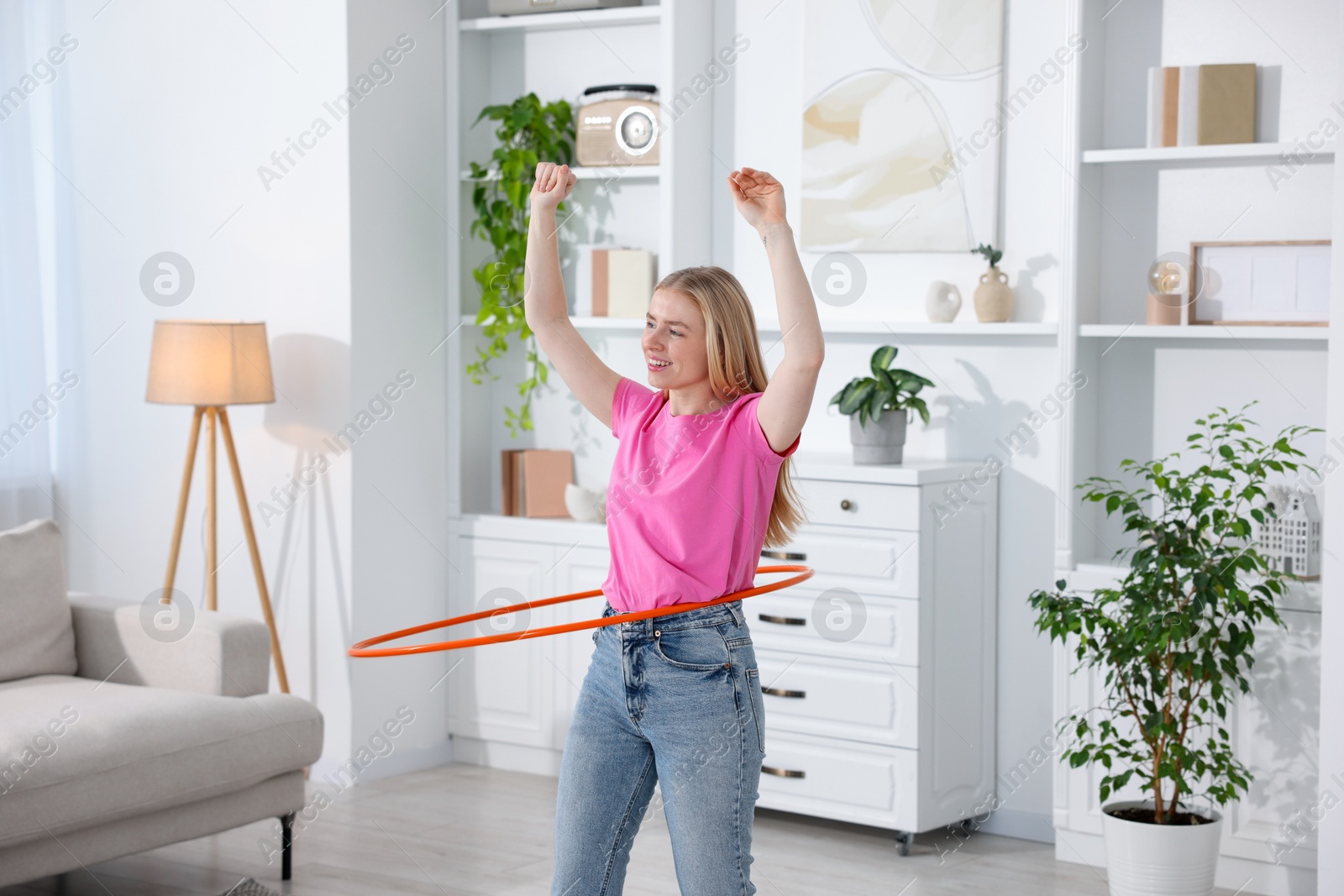 Photo of Beautiful young woman exercising with hula hoop at home