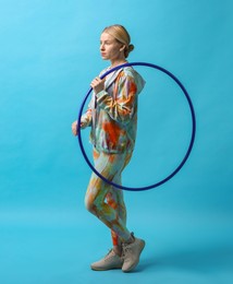 Photo of Beautiful young woman with hula hoop on light blue background, space for text