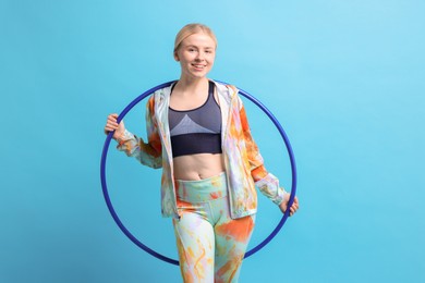 Beautiful young woman with hula hoop on light blue background