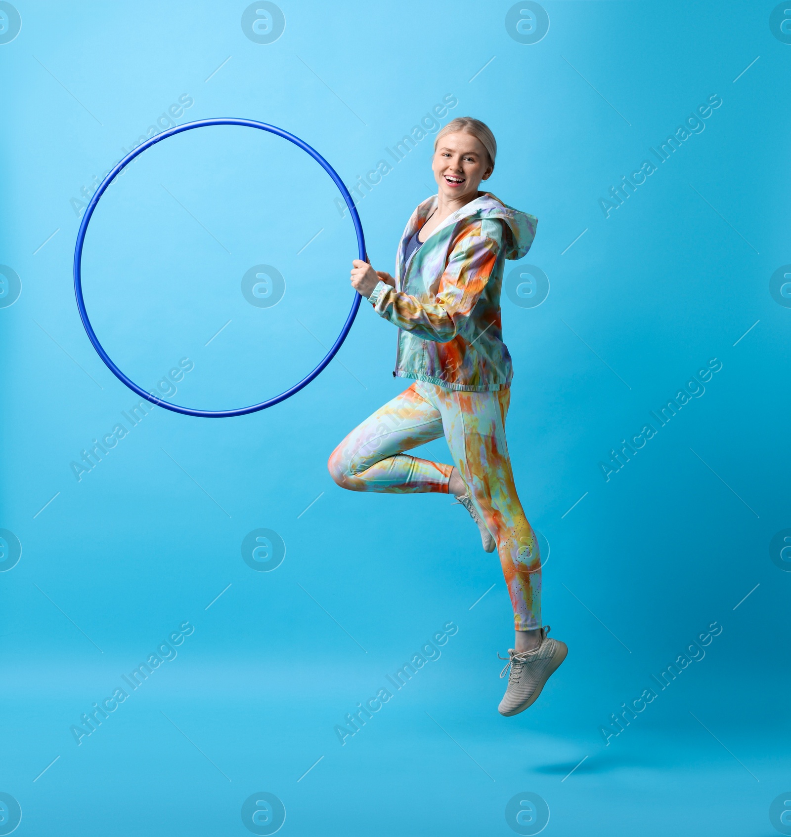 Photo of Beautiful young woman exercising with hula hoop on light blue background