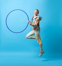 Photo of Beautiful young woman exercising with hula hoop on light blue background