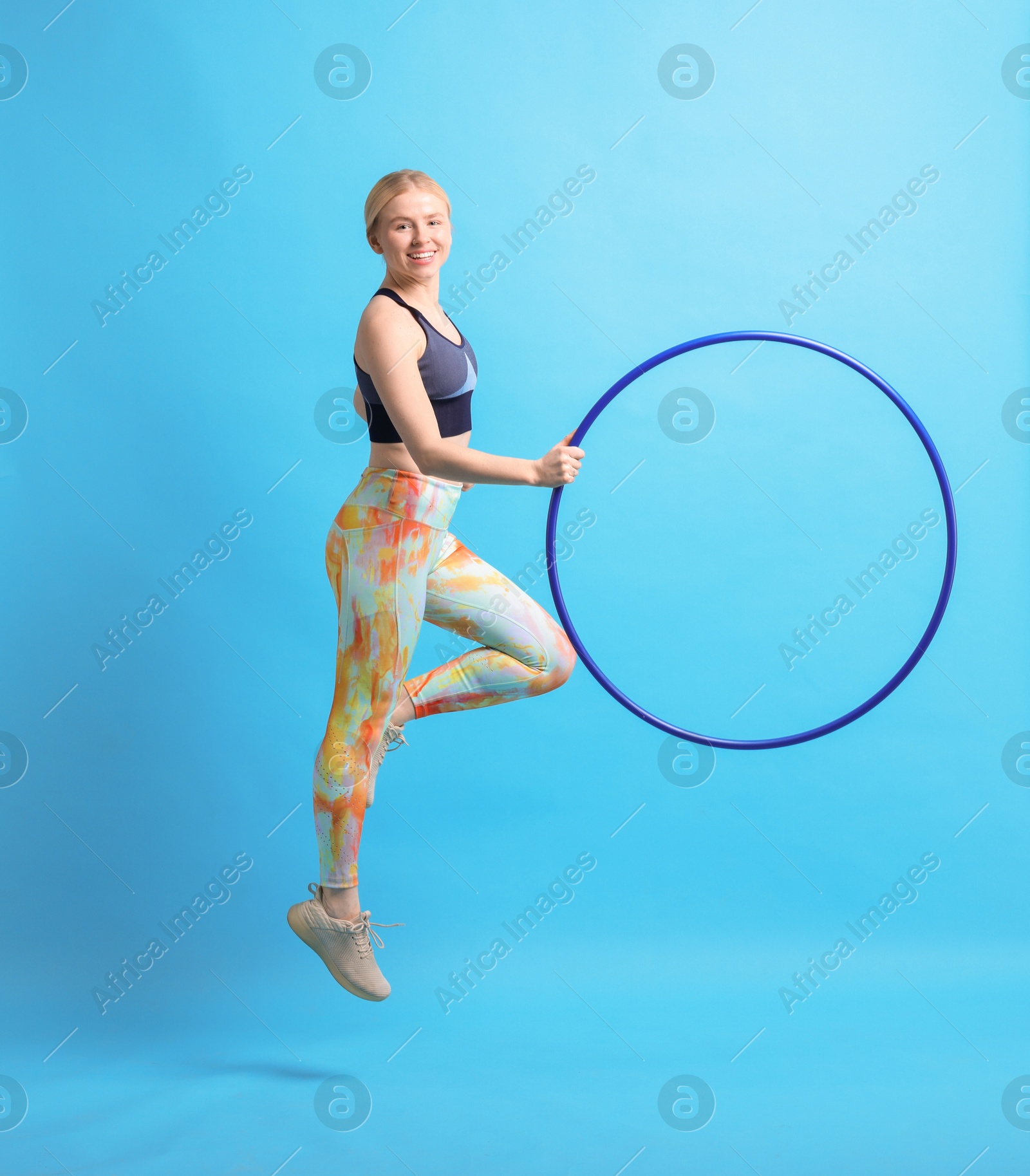 Photo of Beautiful young woman exercising with hula hoop on light blue background