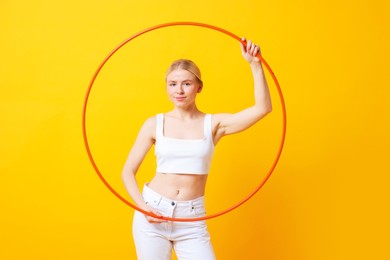 Beautiful young woman with hula hoop on yellow background