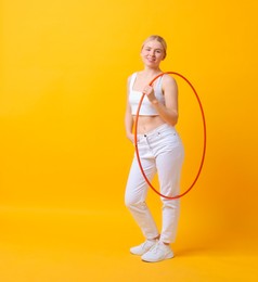 Beautiful young woman with hula hoop on yellow background, space for text