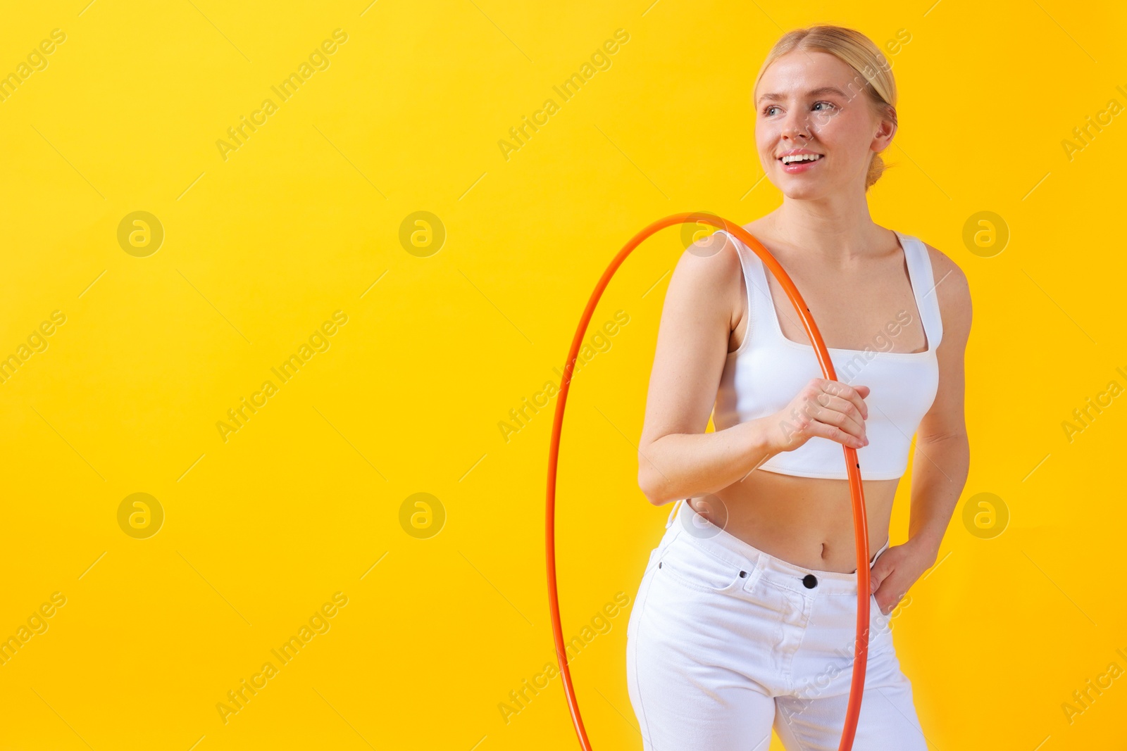 Photo of Beautiful young woman with hula hoop on yellow background, space for text