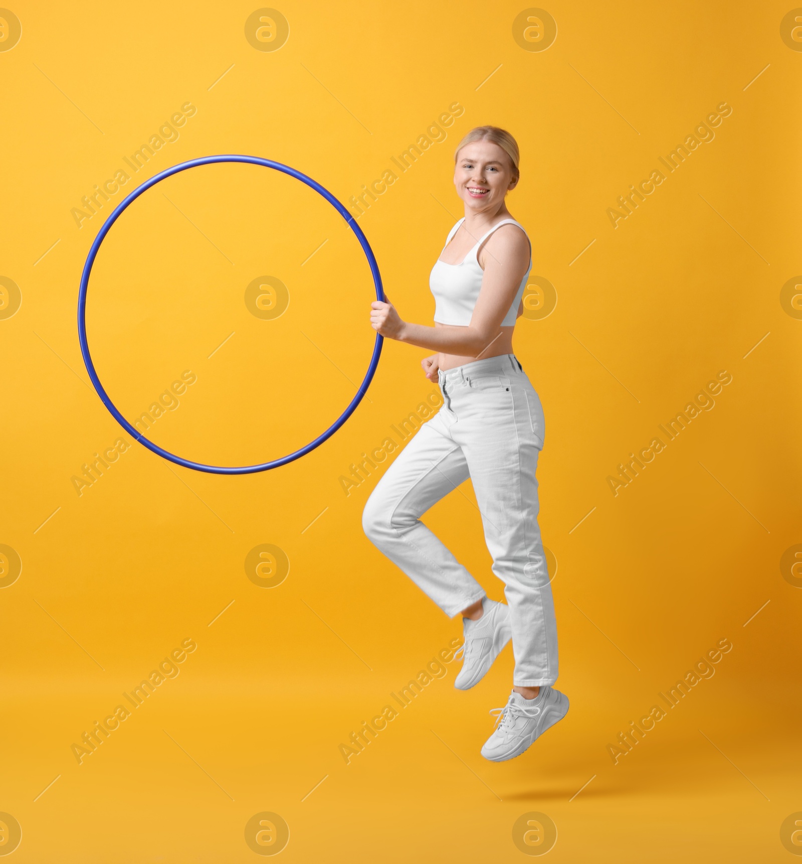 Photo of Beautiful young woman exercising with hula hoop on yellow background, space for text