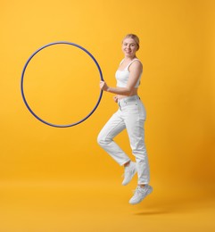 Beautiful young woman exercising with hula hoop on yellow background, space for text