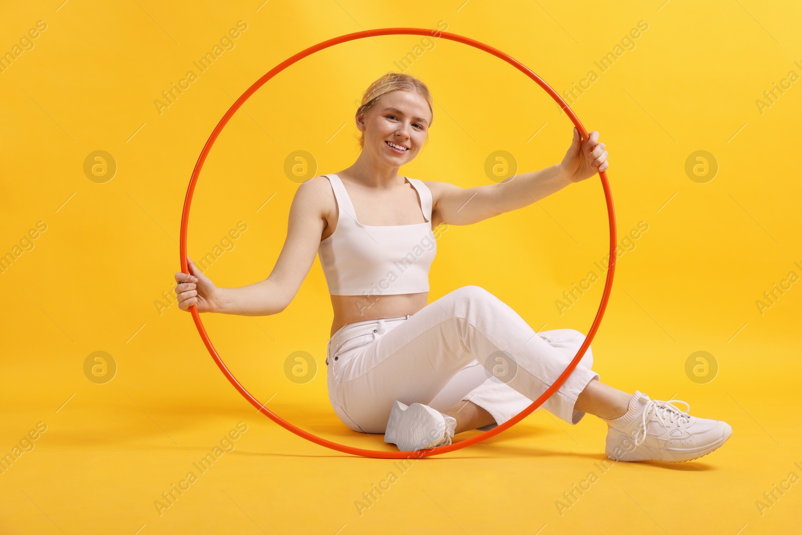 Photo of Beautiful young woman with hula hoop on yellow background