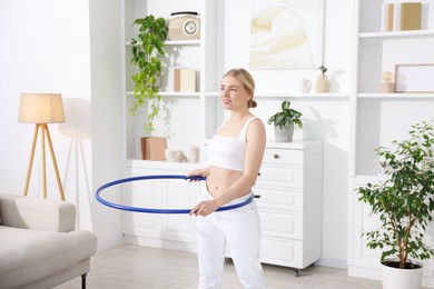 Beautiful young woman exercising with hula hoop at home