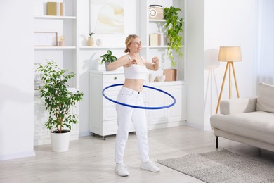 Photo of Beautiful young woman exercising with hula hoop at home