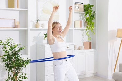 Beautiful young woman exercising with hula hoop at home