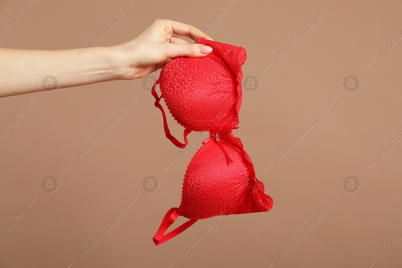 Photo of Woman holding red bra on dark beige background, closeup. Space for text