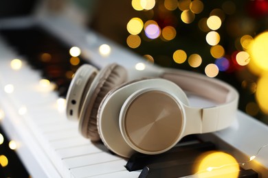 Photo of Headphones on electric piano against blurred lights, closeup. Bokeh effect