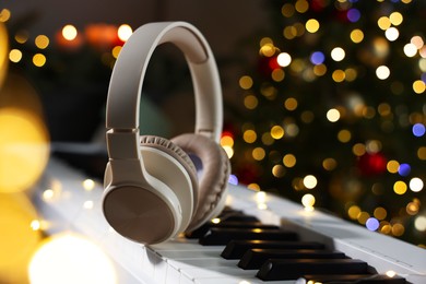 Photo of Headphones on electric piano against Christmas tree with blurred lights, closeup. Bokeh effect