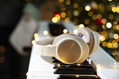 Photo of Headphones on electric piano against Christmas tree with blurred lights, closeup. Bokeh effect