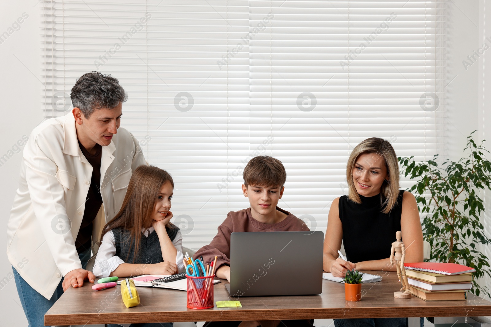 Photo of Parents and their children doing homework with laptop at table indoors