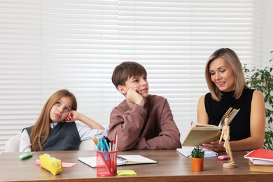 Photo of Smiling mother helping her children with homework at table indoors