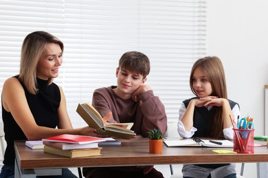 Smiling mother helping her children with homework at table indoors