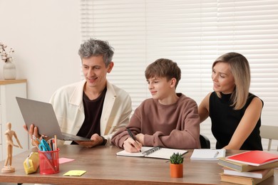 Photo of Smiling parents helping their son with homework at table indoors