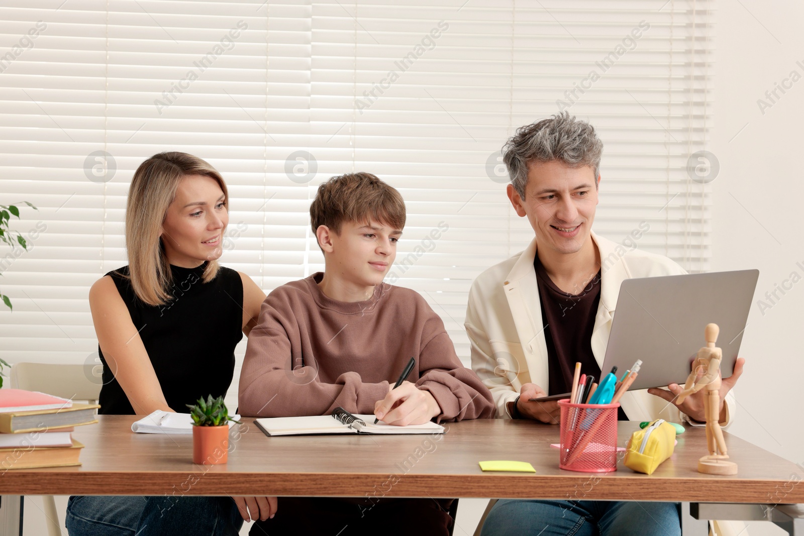 Photo of Smiling parents helping their son with homework at table indoors