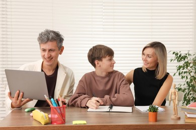 Smiling parents helping their son with homework at table indoors