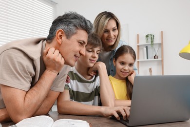 Photo of Parents and their children doing homework with laptop at table indoors