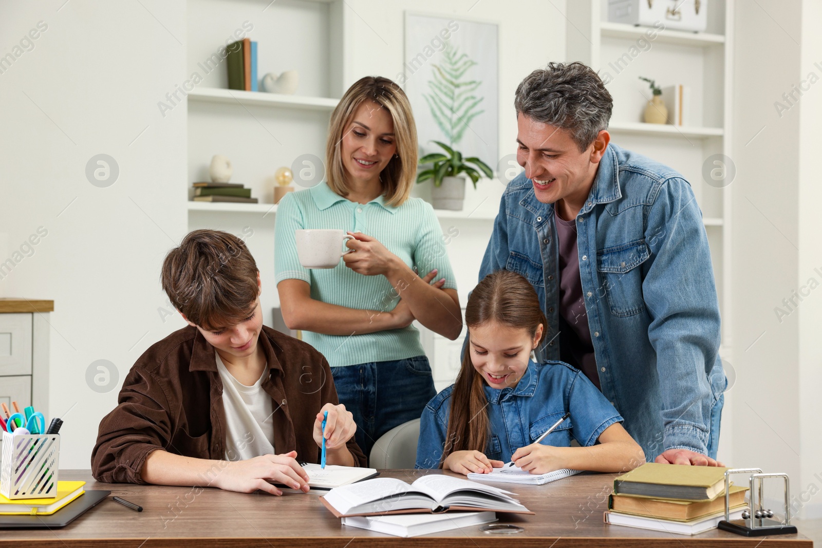 Photo of Smiling parents helping their children with homework at table indoors