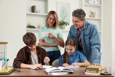 Smiling parents helping their children with homework at table indoors