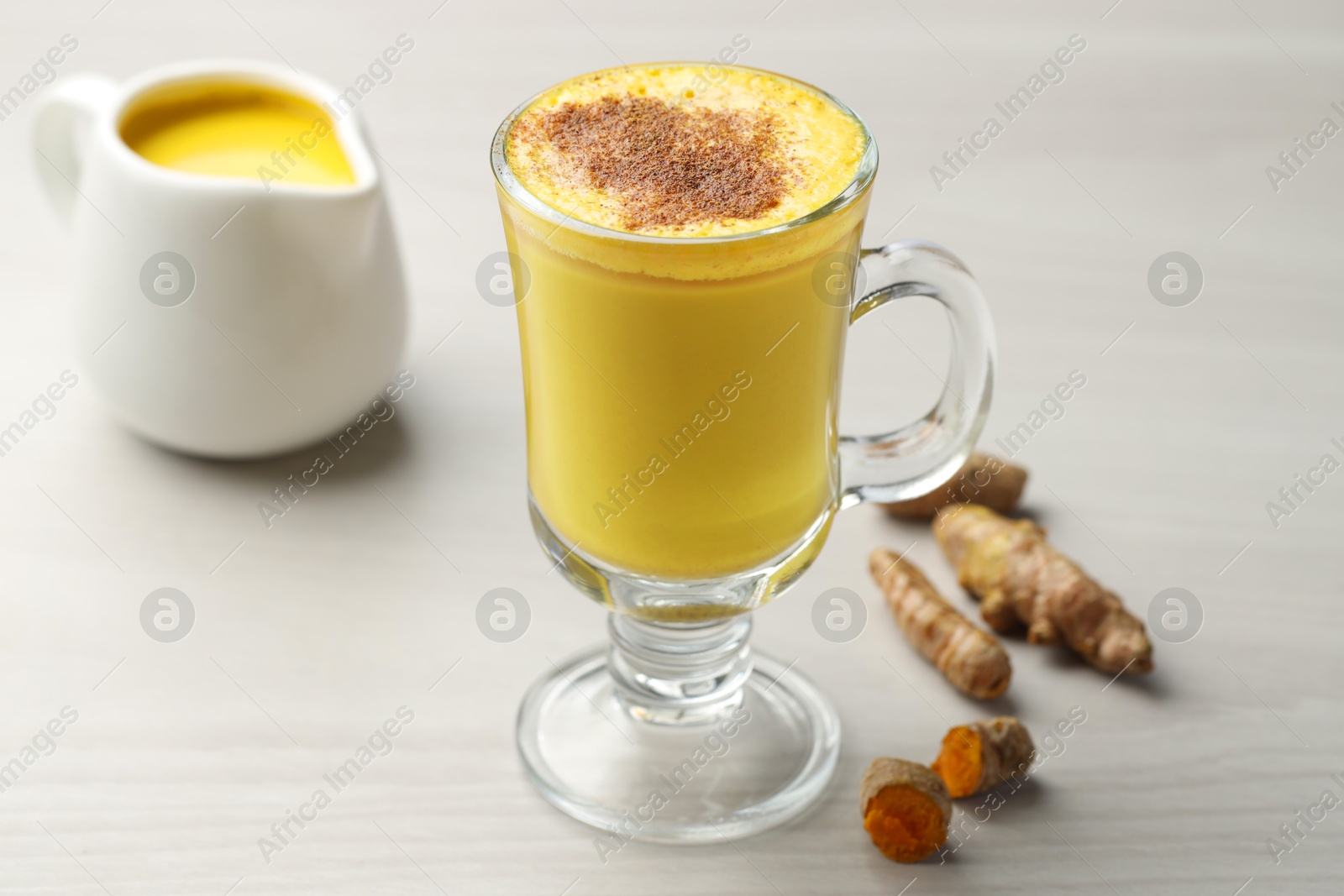 Photo of Delicious turmeric latte and rhizomes on white wooden table, closeup