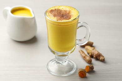 Photo of Delicious turmeric latte and rhizomes on white wooden table, closeup