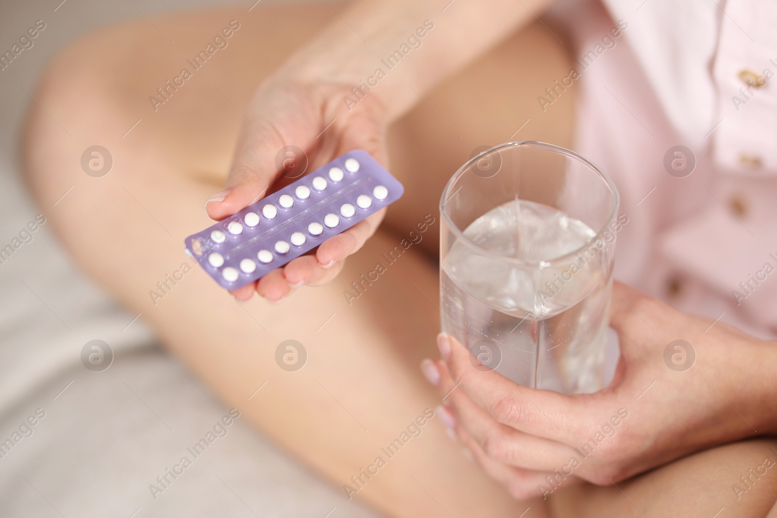 Photo of Woman with contraceptive pills and glass of water on bed, closeup