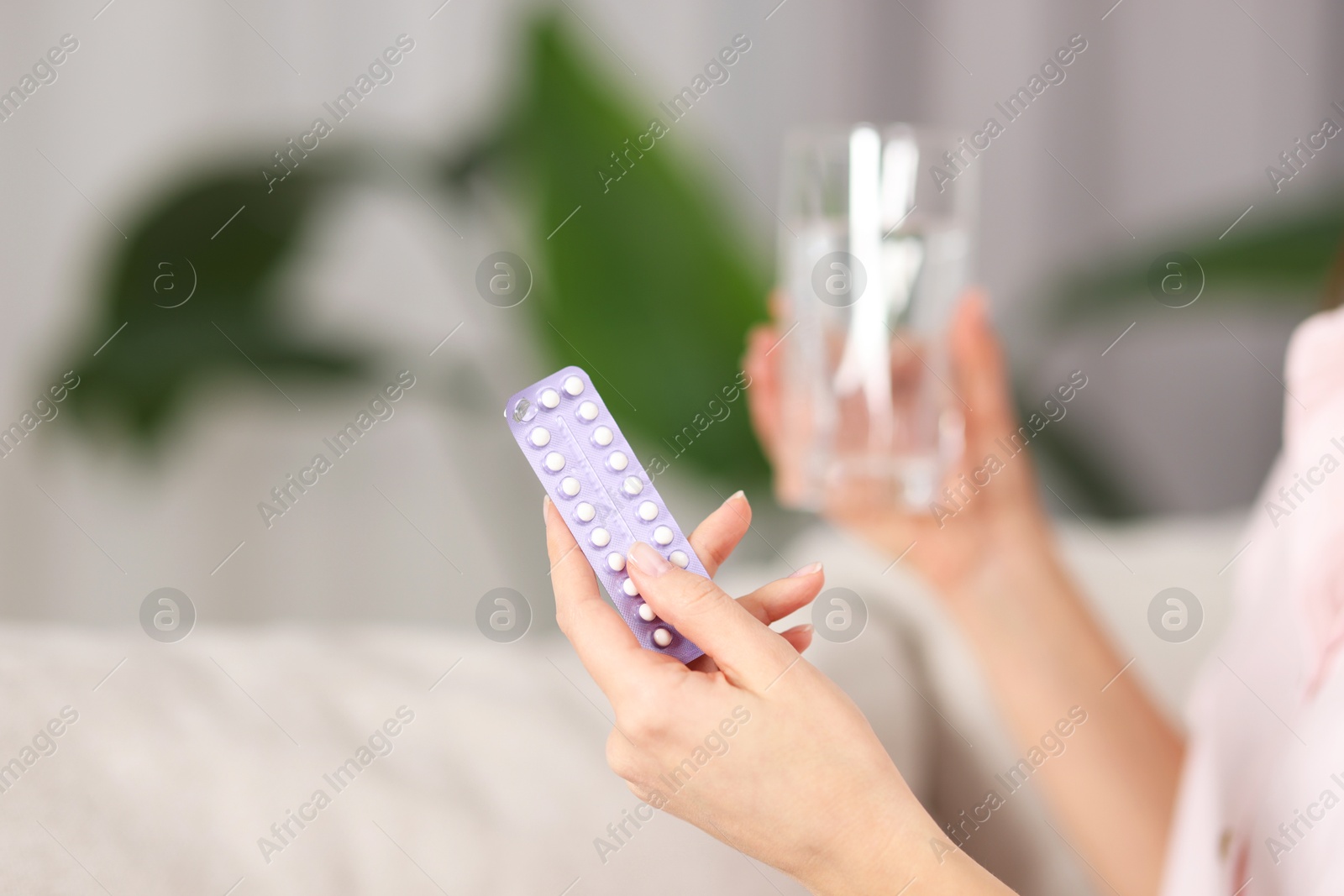 Photo of Woman with contraceptive pills and glass of water indoors, closeup