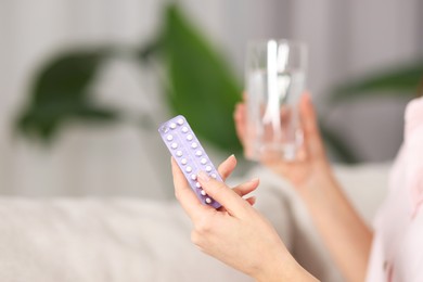 Woman with contraceptive pills and glass of water indoors, closeup