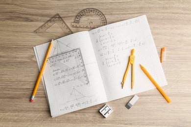 Doing homework. Copybook with math assignment and different stationery on wooden table, flat lay