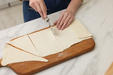 Photo of Woman cutting dough at light marble table indoors, closeup. Making croissants