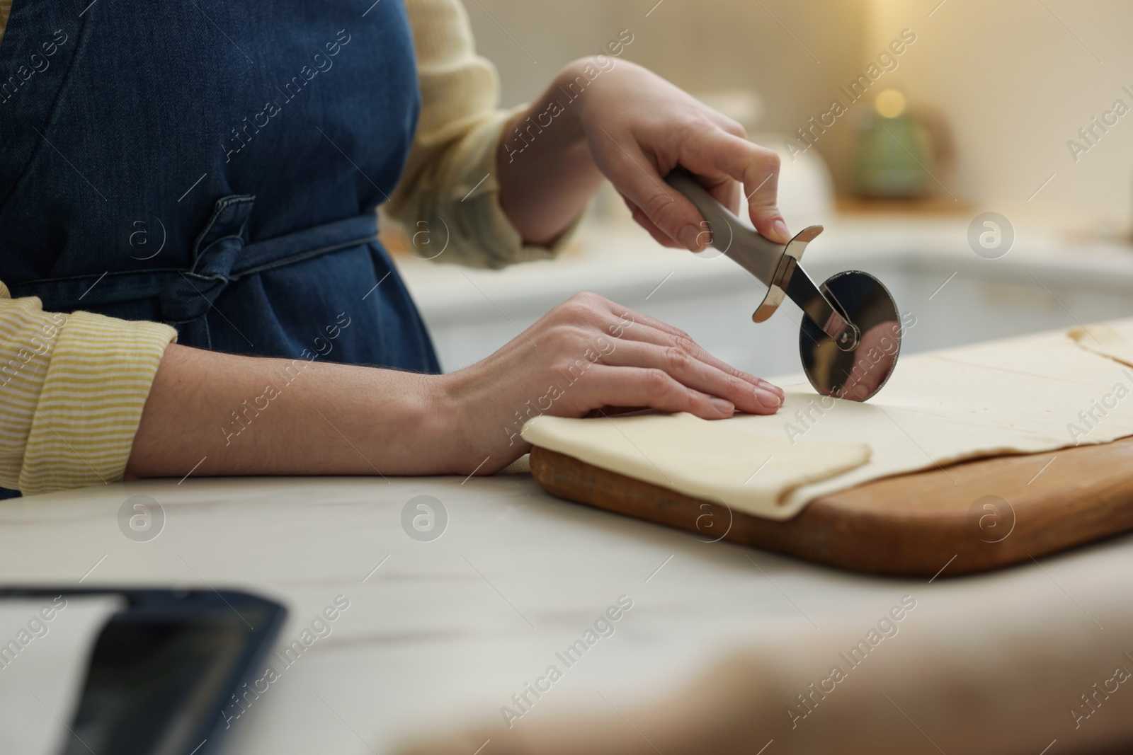 Photo of Woman cutting dough at light marble table indoors, closeup. Making croissants