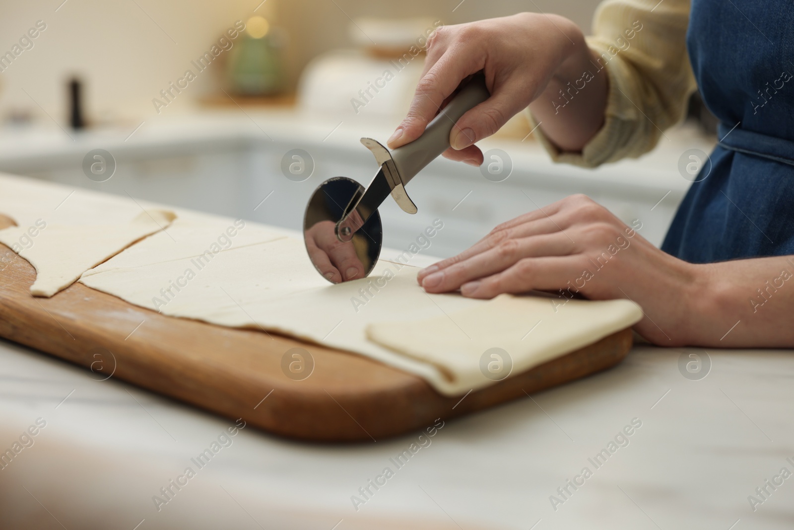 Photo of Woman cutting dough at light marble table indoors, closeup. Making croissants