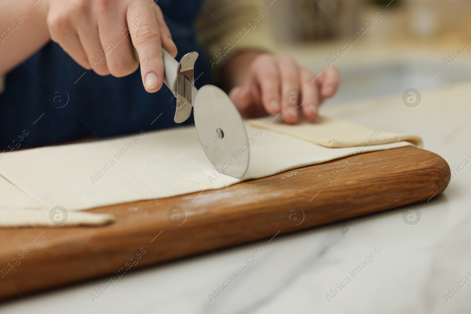 Photo of Woman cutting dough at light marble table indoors, closeup. Making croissants