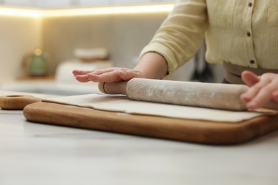 Woman rolling dough at light table indoors, closeup. Making croissants