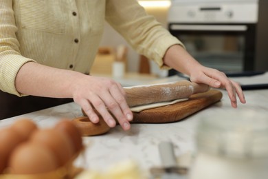 Photo of Woman rolling dough at light marble table indoors, closeup. Making croissants