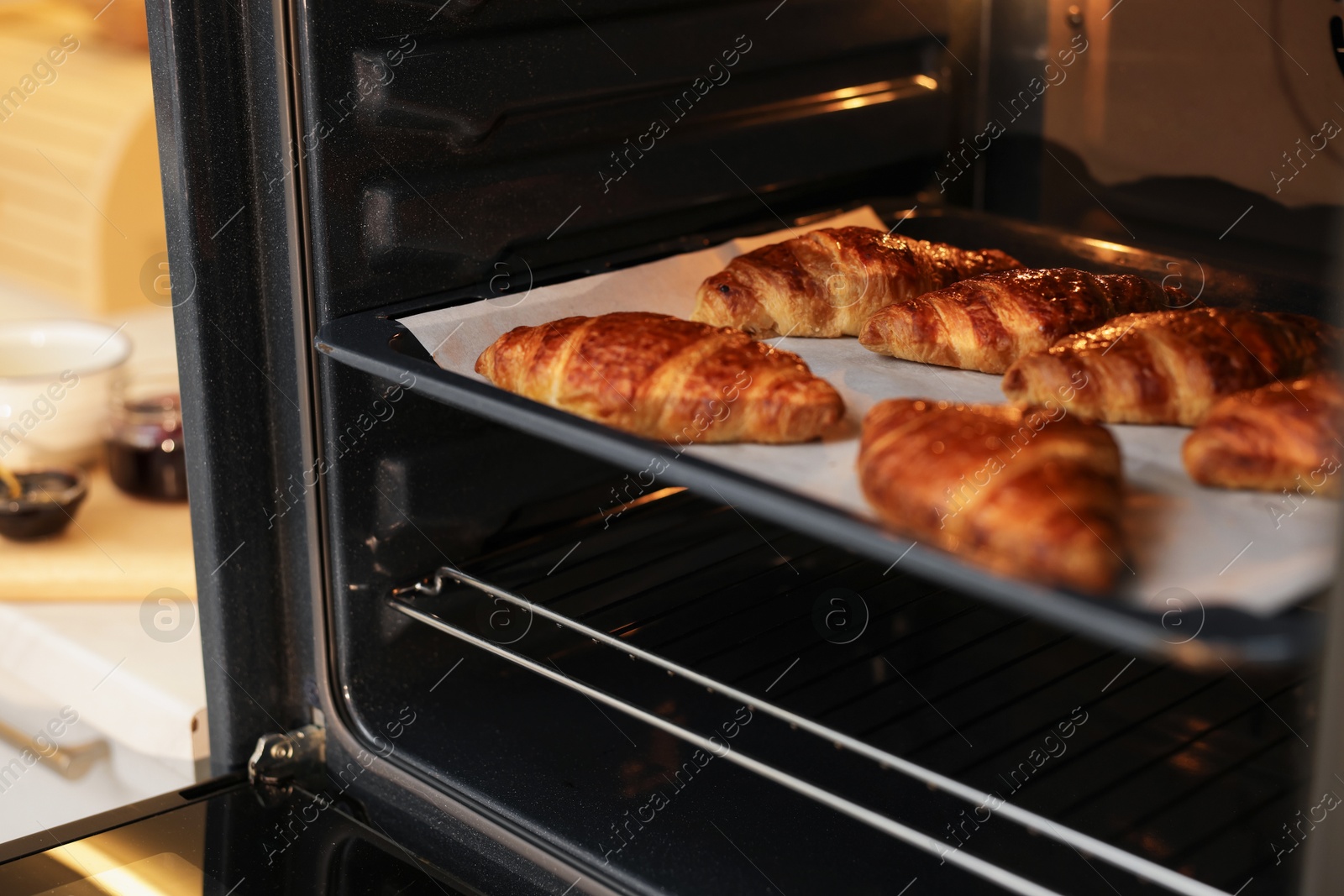 Photo of Freshly baked croissants on baking sheet in oven indoors, closeup