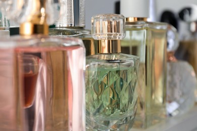 Photo of Different aromatic perfumes in bottles on shelf, closeup