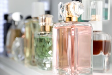 Photo of Different aromatic perfumes in bottles on shelf, closeup