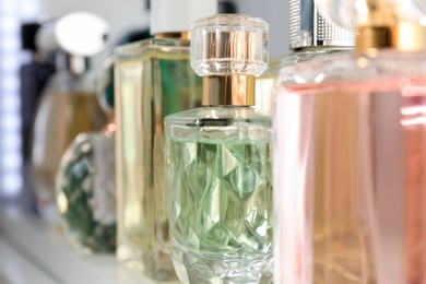 Photo of Different aromatic perfumes in bottles on shelf, closeup